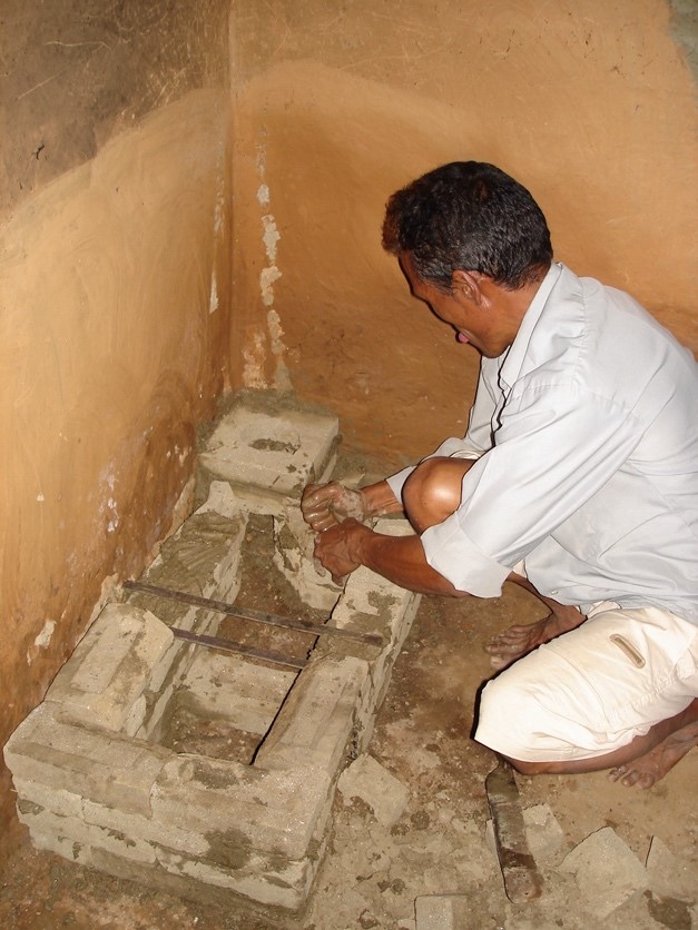 Ein Ofenbauer hockt vor dem Fundament eines neuen Lehmofens und beginnt, den Schornstein zu setzen.
