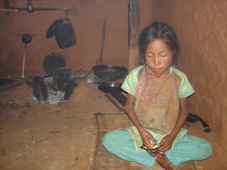 Das Mädchen Sanu Maya sitzt traurig vor der gelöschten Feuerstelle im Innern ihres Hauses.